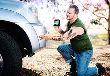 A man with tattoos proposing to his car with a Soapy Joe's air freshener.