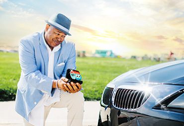 A man in a suit and hat proposing to his car with a Soapy Joe's air freshener.