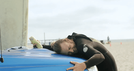A man in a wetsuit on the beach hugging his car.